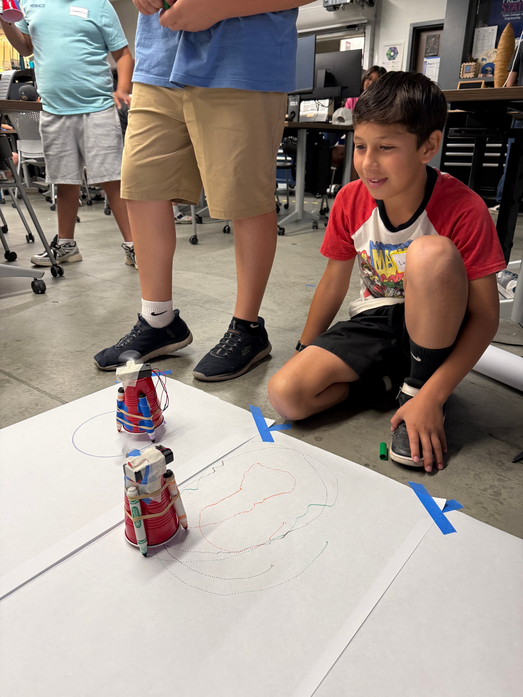 Student watching two vibrating art robots draw during an early test