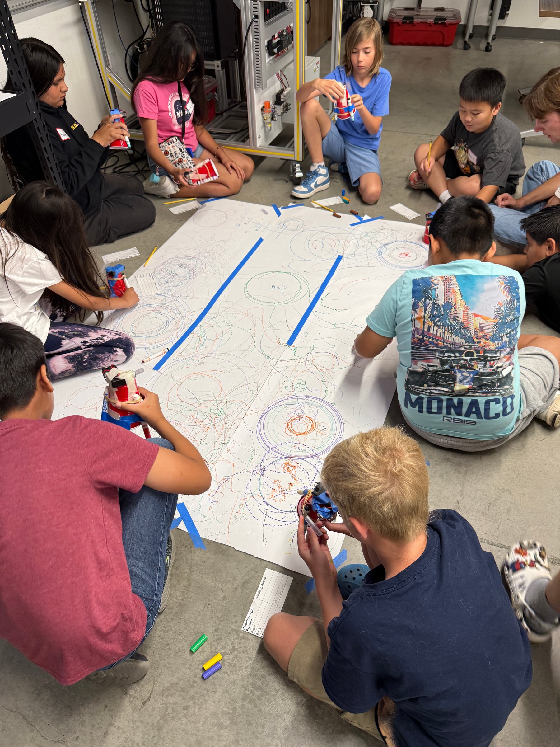 Students gathered around two large paper rolls while testing their vibrating art robots